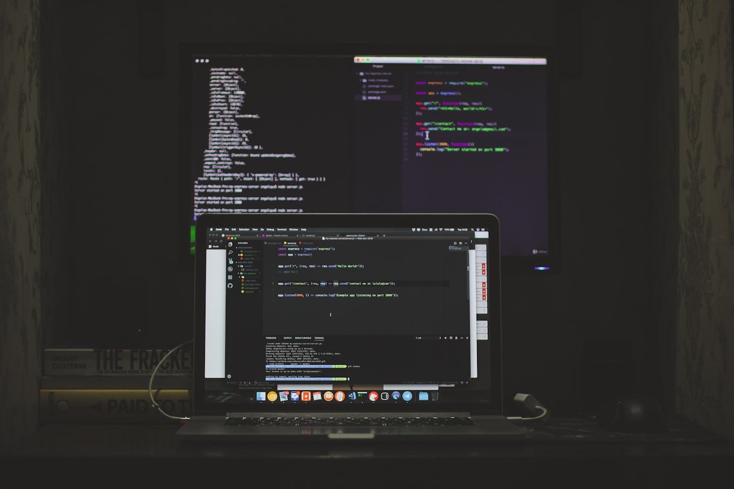 Laptop and external monitor displaying code on a desk.